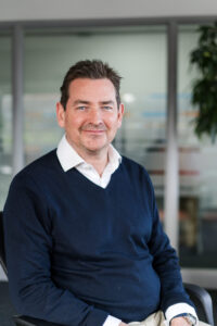 Headshot of Nexus CEO sitting on a chair with a blurred office background.