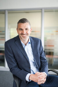 Headshot of Nexus Chief Revenue Officer sat on a chair on blurred office background